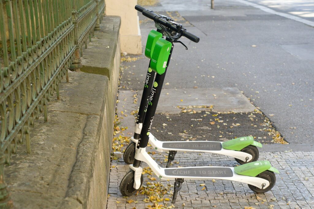 Dvě elektrické koloběžky společnosti Lime zaparkované na chodníku vedle plotu